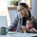 Mother holding baby and working at her computer